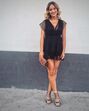 Mulher sorri com vestido preto, clutch e sandálias de salto alto