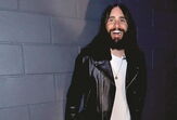 Jared Leto sorri com casaco de cabedal preto