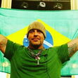 Homem com gorro e tatuagens exibe a bandeira do Brasil