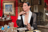 Mulher sorri à mesa com joias e decoração clássica