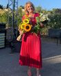 Mulher sorridente segura dois ramos de flores num evento ao ar livre