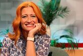 Mulher sorri com cabelo ruivo, blusa estampada e relógio