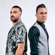 Dois homens posam juntos com visuais distintos.
