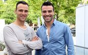 Dois homens sorriem lado a lado num dia ensolarado