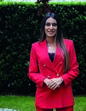 Mulher com blazer vermelho posa sorridente num jardim