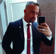 Homem de fato e gravata vermelha tira selfie no espelho