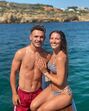 Um casal sorri num passeio de barco, com o mar e falésias no fundo