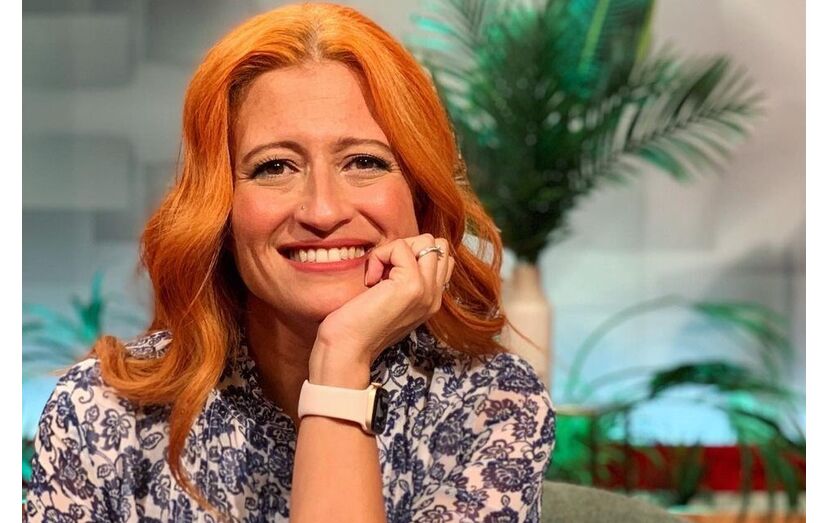 Mulher sorri com cabelo ruivo, blusa estampada e relógio