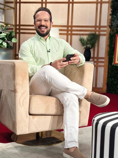 Homem sorridente e relaxado, sentado numa cadeira com um telemóvel na mão