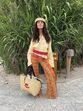 Mulher posa com calças aos quadrados, blusa amarela e mala de praia "AMI Paris"