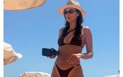 Mulher de biquíni e chapéu desfruta de dia na praia sob o sol