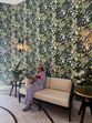Mulher relaxa num sofá num espaço decorado com papel de parede floral