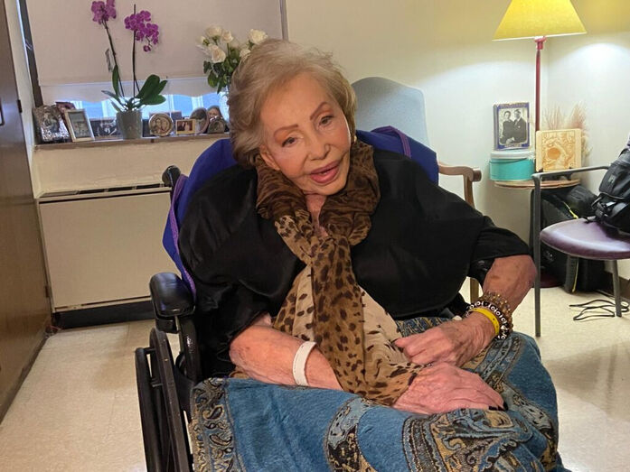 Mulher sorri numa cadeira de rodas, com um lenço com padrão de leopardo
