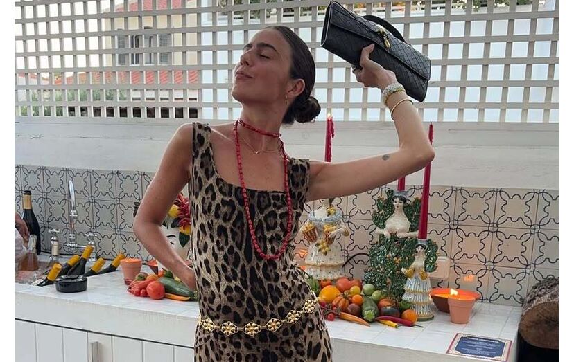 Mulher posa com vestido estampado, colar e mala preta