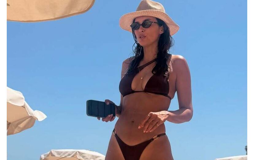Mulher de biquíni e chapéu desfruta de dia na praia sob o sol