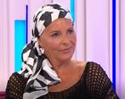 Mulher com lenço na cabeça sorri num estúdio de televisão
