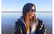 Mulher de óculos escuros e casaco de cabedal perto de um lago aproveita o dia ensolarado