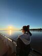 Mulher observa o pôr do sol no mar, de óculos e casaco