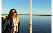 Mulher sorri junto à bandeira do Uruguai com vista para o mar
