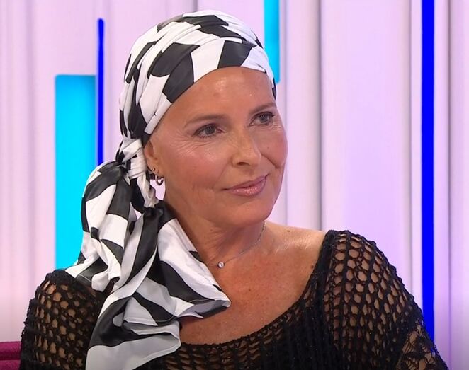 Mulher com lenço na cabeça sorri num estúdio de televisão