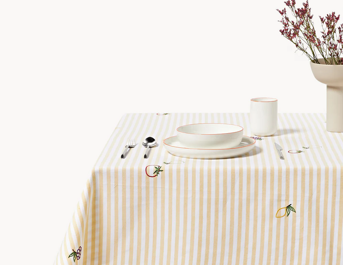 Mesa de jantar elegante com louça branca, toalha às riscas e decoração floral