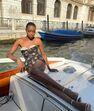 Maria Borges relaxa num barco em Veneza com um vestido floral elegante.

