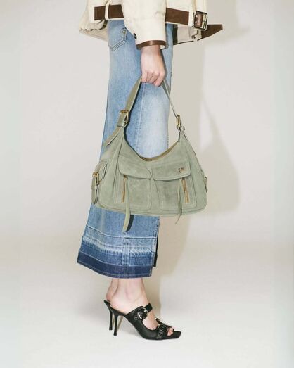 Mulher exibe mala de camurça verde-acinzentada, jeans e mules pretas de salto alto