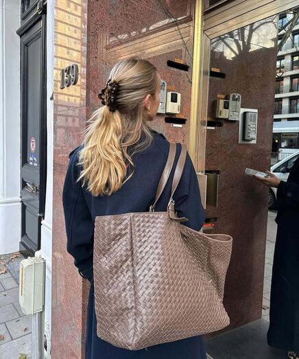 Mulher com mala grande espera para entrar num edifício.
