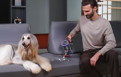 Homem usa aspirador no sofá perto de cão afegão