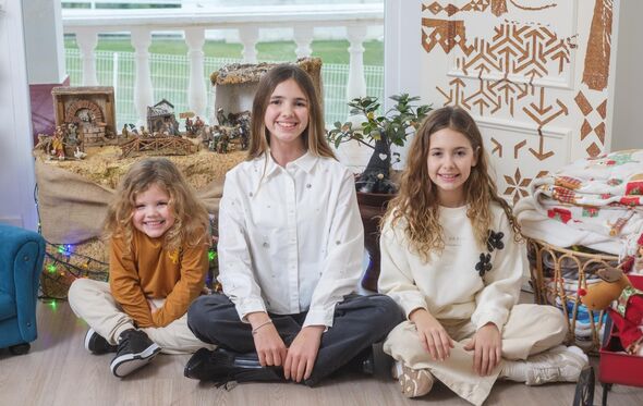 Três meninas sorriem junto a presépio e decorações natalícias