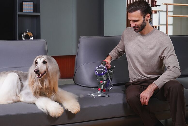 Homem usa aspirador no sofá perto de cão afegão