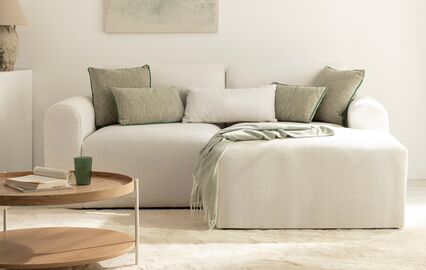 Sala de estar luminosa com sofá, almofadas e mesa de apoio, criando um ambiente elegante e acolhedor.
