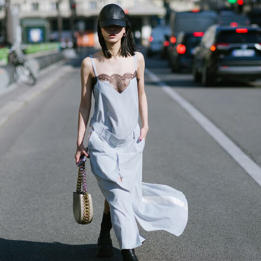 Mulher com vestido azul e boné de cabedal numa rua em Paris