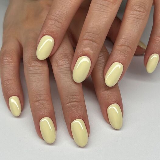 Mãos com unhas pintadas de amarelo pastel mostram tendência de manicure