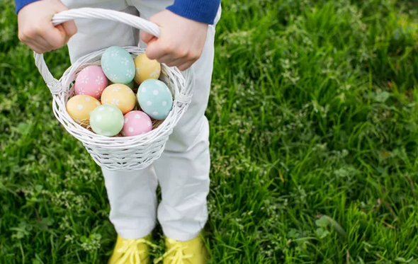 Criança segura cesto com ovos coloridos na caça aos ovos da Páscoa