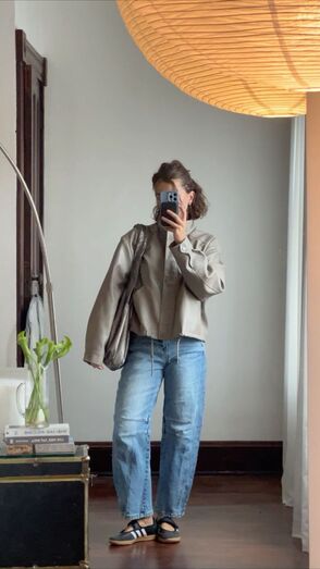 Uma pessoa tira uma selfie com um casaco bege, calças de ganga e sapatos pretos