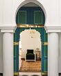 Porta colorida em arco com detalhes dourados, colunas brancas e sala de estar