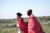 Homem e mulher Masai com vestes tradicionais caminham pela paisagem do Quénia