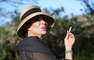 Mulher com chapéu de palha fuma cigarro com pulseiras douradas