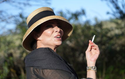 Mulher com chapéu de palha fuma cigarro com pulseiras douradas
