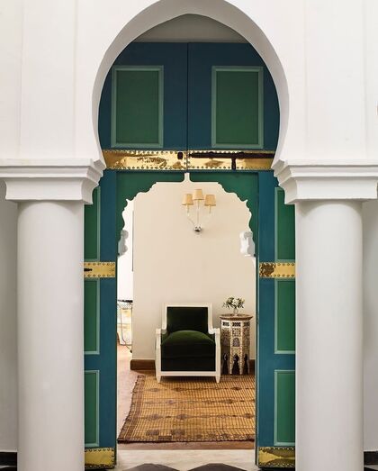 Porta colorida em arco com detalhes dourados, colunas brancas e sala de estar