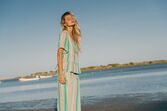 Mulher de cabelo loiro, de olhos fechados, usa um vestido às riscas coloridas numa praia