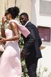 Casal desfila em evento, ele de fato e ela de vestido rosa