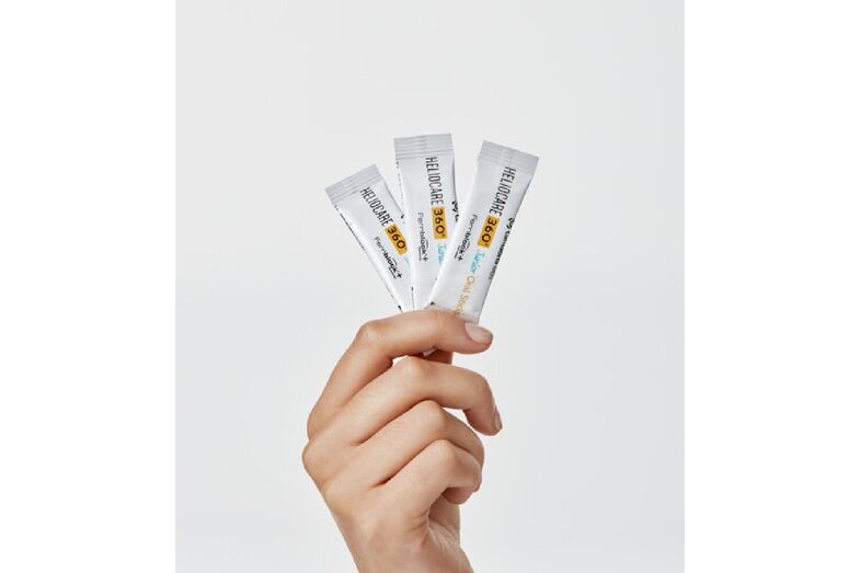 Mão segura 3 ampolas de Heliocare 360º Junior Oral Sticks