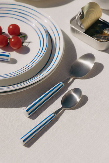Mesa posta no exterior com pratos listrados, tomate e sardinhas em lata