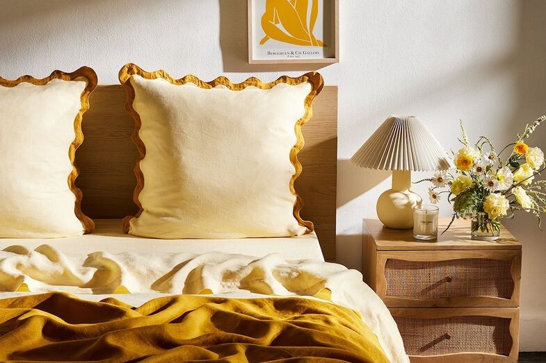 Quarto com lençóis amarelos, candeeiro e arranjo de flores