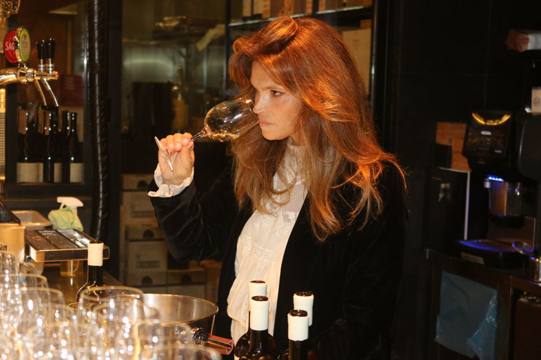 Mulher com cabelo ruivo avalia um copo de vinho branco